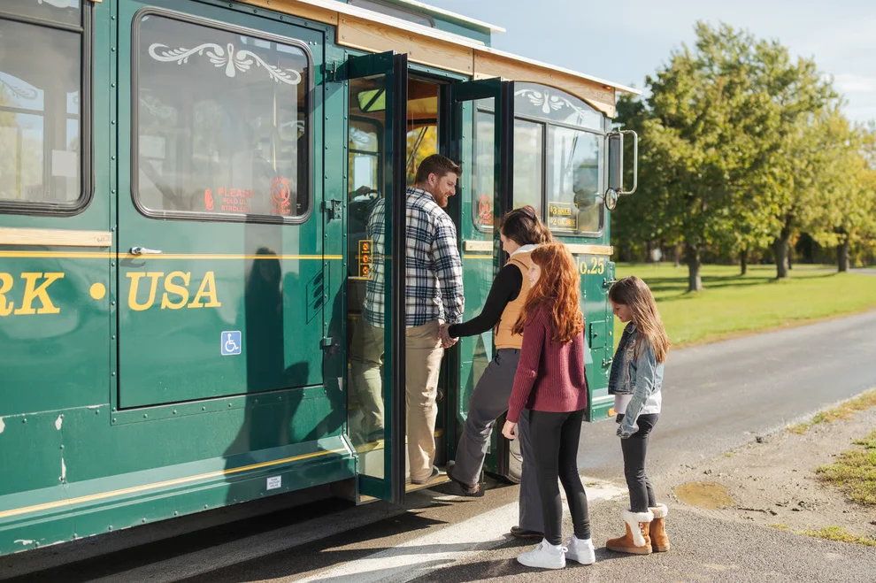 A family boarding a green Niagara Falls Trolley on a sunny day surrounded by trees and an open grassy area