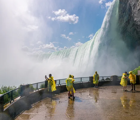 Visitors in yellow ponchos experiencing the power of Niagara Falls up close at Journey Behind the Falls, surrounded by the mist and majesty of the cascading waters