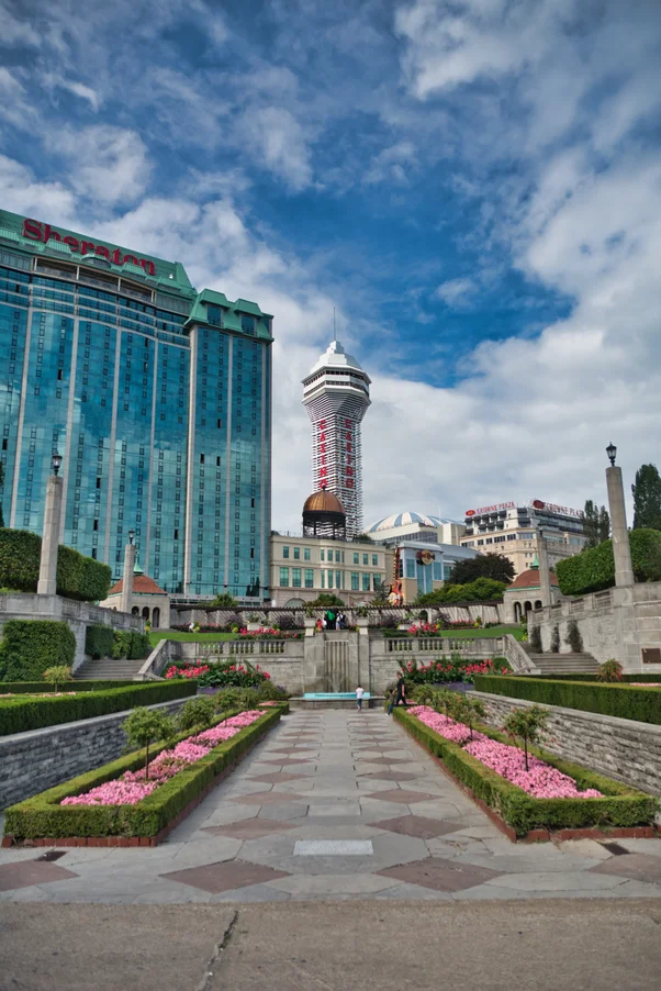Oakes Garden Theatre main pathway with beautifully maintained hedges, colorful flowers, and luxury hotels in the background under a bright blue sky