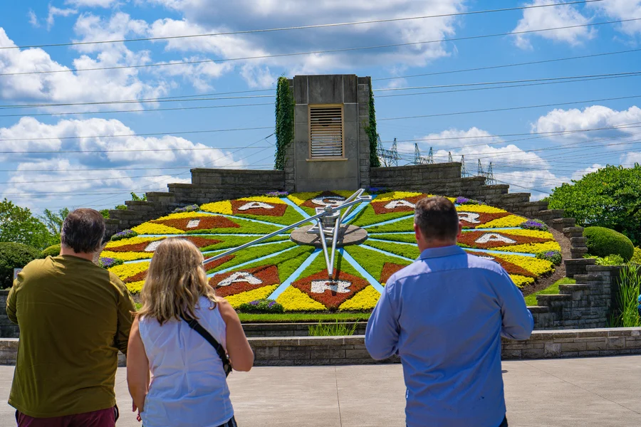 Visitors admiring the beautiful summer floral clock display with thousands of colorful seasonal blooms arranged in a giant working timepiece
